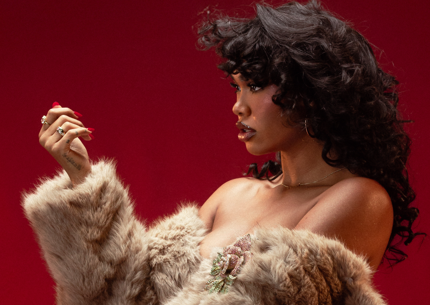 Musician Amber Mark facing right looking at her hand in front of red backdrop.x